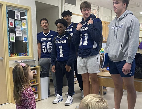 Preschool students looking up to PHS football players during their visit